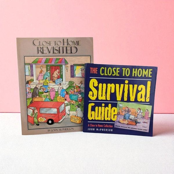 Two softcover cartoon collection books by John McPherson. One book has a tan cover featuring a crowded house scene with a red van. The second book is navy blue with bold yellow and white text and a living room cartoon.