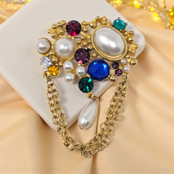 An ornate vintage gold-tone brooch and chatelaine pin set, featuring a colorful mix of multi-sized faux pearls and large red, blue, green, and purple rhinestones. A double gold chain with a teardrop pearl dangle connects the two pieces.