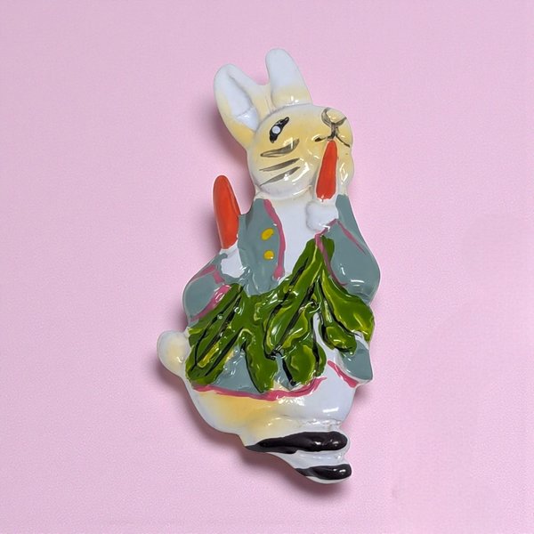A 1.5-inch vintage brooch featuring a whimsical rabbit in a leaping or sitting pose. The piece is finished with smooth, high-shine enamel—typically in a classic white or pastel spring shade—over a gold-tone base. It features a polished silhouette with a delicate, rounded form and a secure pin-back closure.