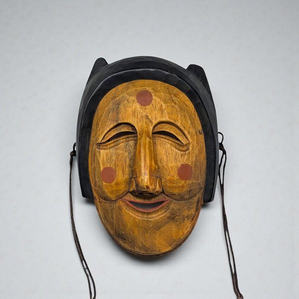 A hand-carved wooden mask with a deep mahogany finish. The face features elongated features, slit eyes, and a prominent nose, with subtle geometric patterns etched along the forehead and cheeks.