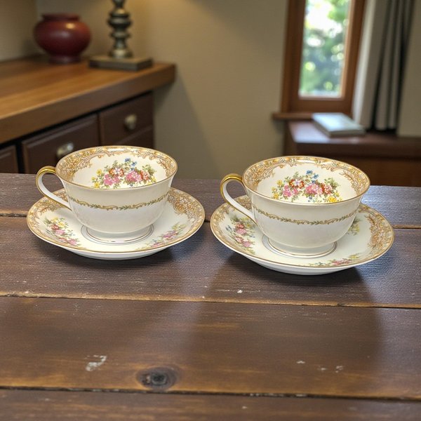 A matched pair of delicate porcelain tea cups and saucers. Each cup features a classic flared rim and a slender handle, resting upon a circular saucer with a gentle upward curve. The porcelain is a crisp, brilliant white with a high-gloss finish.
