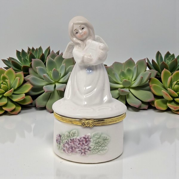 A slender white ceramic figurine of an angel playing a gold-accented harp. The base of her gown is decorated with delicate purple floral sprigs and opens to reveal a small storage compartment.