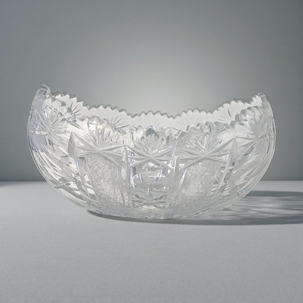 A heavy, boat-shaped clear crystal bowl featuring deep geometric hand-cut patterns. The surface is covered in intricate starbursts and hobnail textures that create a brilliant prismatic effect.