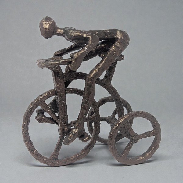 Dark welded metal sculpture of a stylized man pedaling a tricycle. The figure features raw industrial textures, visible weld marks, and a heavy, blackened silhouette.