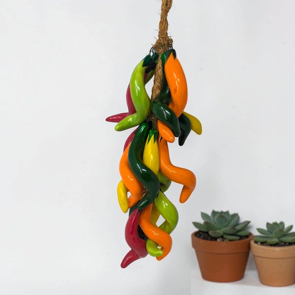 A vertical cluster of glossy ceramic chili peppers in vibrant shades of red, orange, yellow, and green. The peppers feature curved silhouettes and are wired to a thick, twisted natural fiber rope.