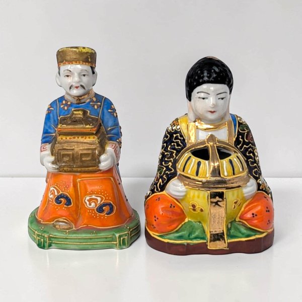 A pair of porcelain figurines depicting people in traditional robes. Both wear robes and a cap.
