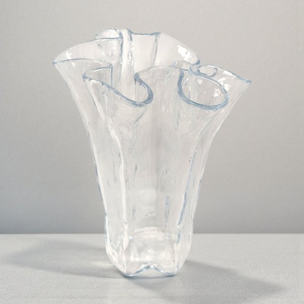 A clear glass vase with a thick, stable base that transitions into a dramatic, fluid ruffled rim. The glass is crystal clear with a high-shine finish, capturing light through its organic, wavy silhouette.