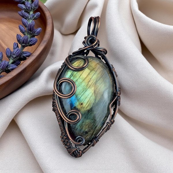 A large teardrop labradorite stone with yellow and green hues. It is wrapped in dark oxidized copper wire featuring three prominent polished spirals on the left side and a woven bail at the top.