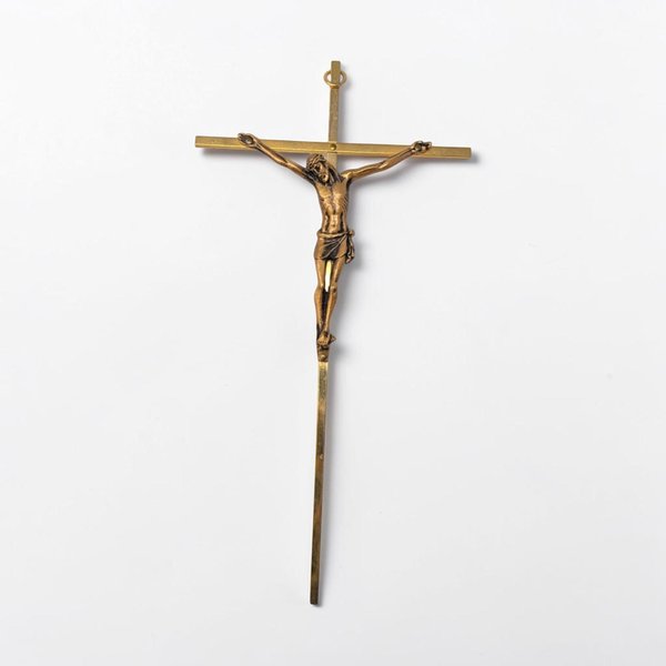 A slender, polished gold-tone metal crucifix with an ornate flared cross design. The figure of Christ is rendered in high relief with a small INRI plaque positioned at the very top of the vertical beam.